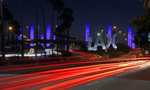 Nighttime image of the sign for LAX, which is close to several nearby card rooms and casinos for gamblers during a layover